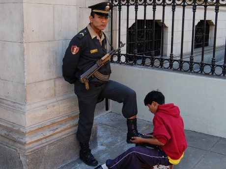 An armed guard getting a quick shoe shine in front of the government building in Central Lima